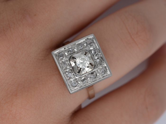 Détail porté d’une bague Art déco carrée en or blanc avec diamant ancien et entourage diamanté