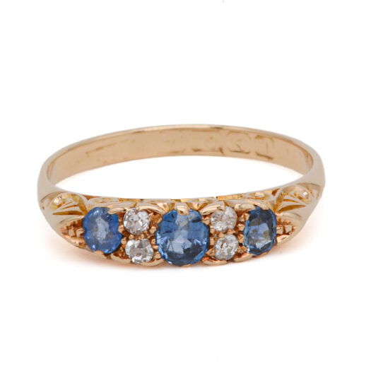 Vue de face d’une bague jarretière ancienne en or jaune sertie de trois saphirs bleus et de quatre diamants taille ancienne.