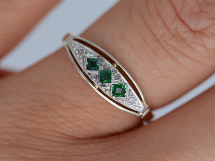 Bague jarretière Art déco en or et pierres vertes portée à la main